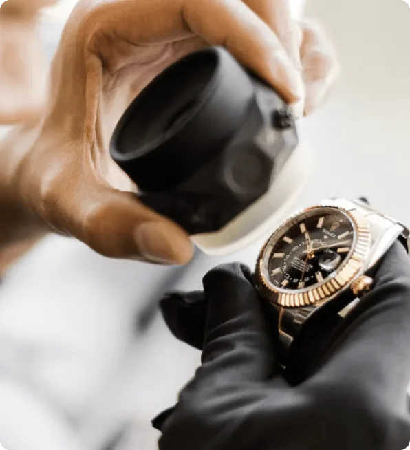 A gloved specialist inspecting a two-tone Rolex with a loupe