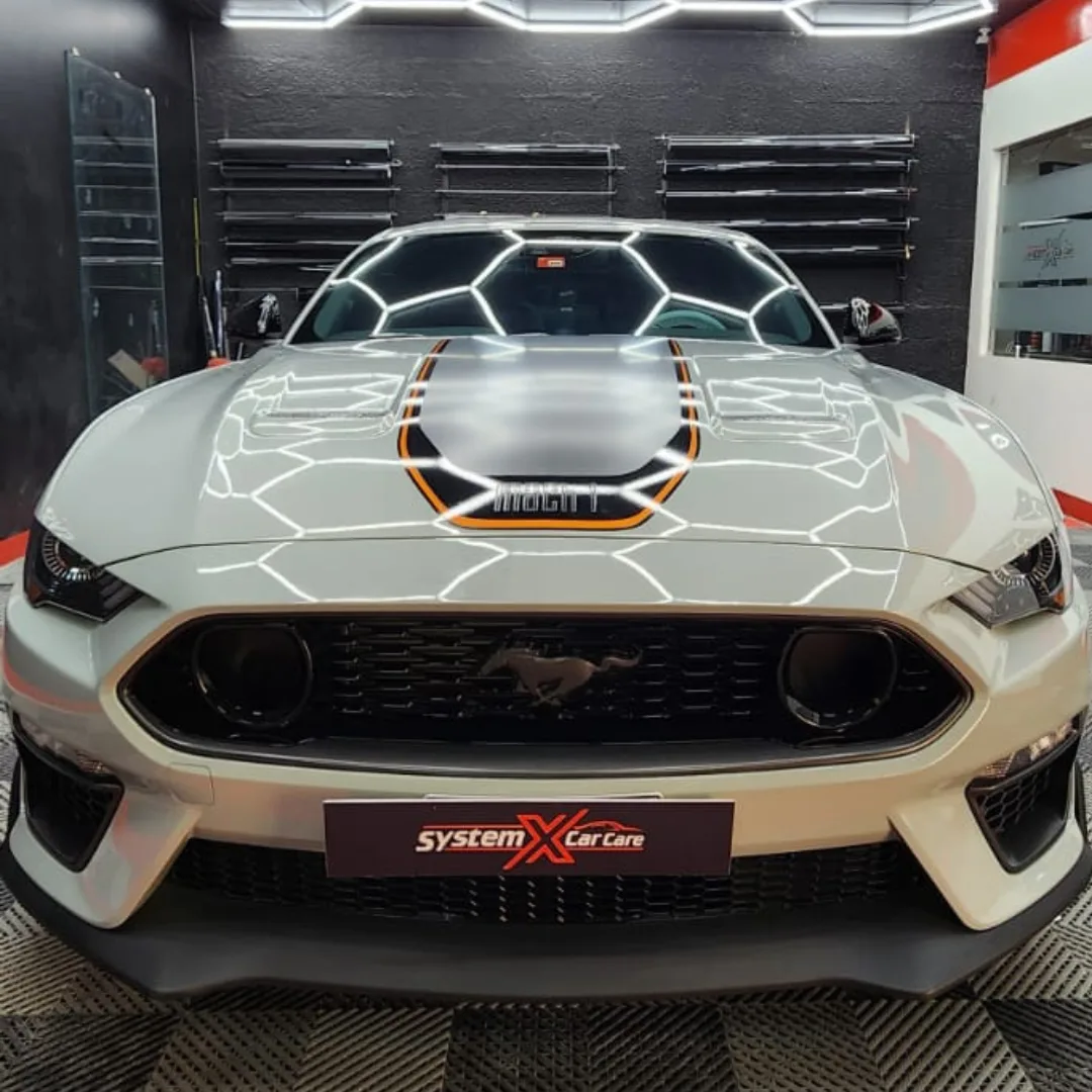 A light grey Ford Mustang detailed under the hexagonal LED bay at System X Car Care, Dubai