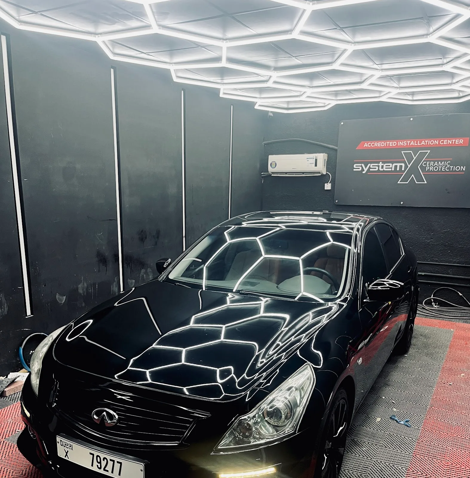 A glossy black car reflecting the hexagonal LED ceiling