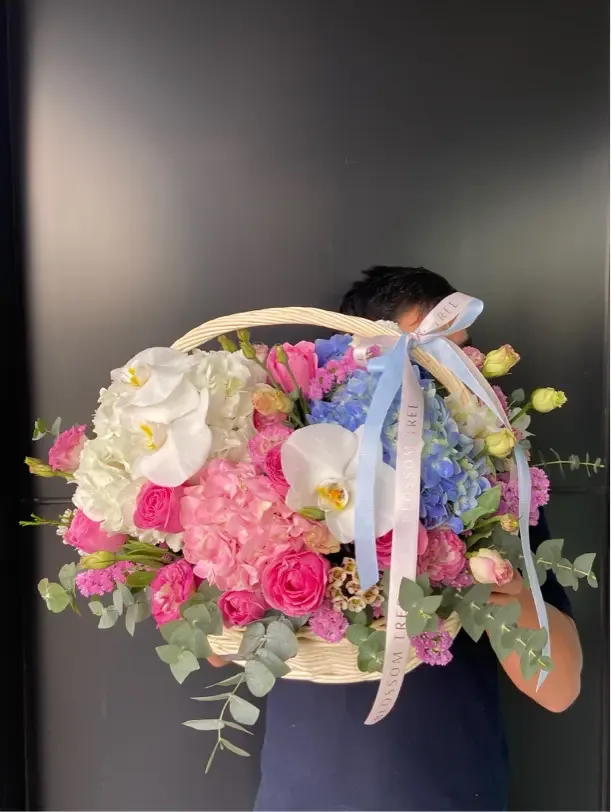 Celebration basket of pink and blue flowers with white orchids