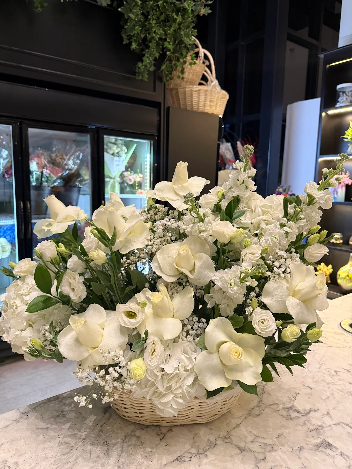 All-white basket arrangement of roses, lisianthus and gypsophila