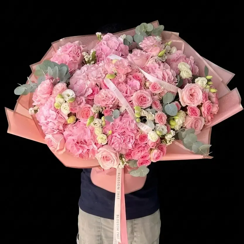 A large hand-tied bouquet of pink hydrangeas and roses wrapped in pink paper