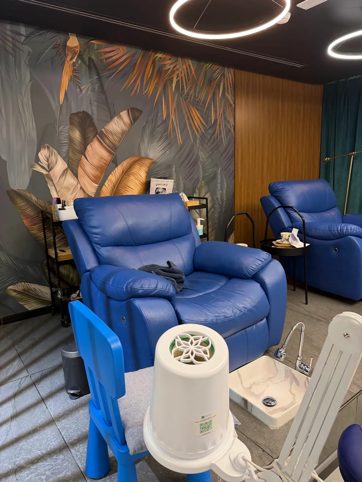 Pedicure lounge with blue recliner chairs and a tropical mural