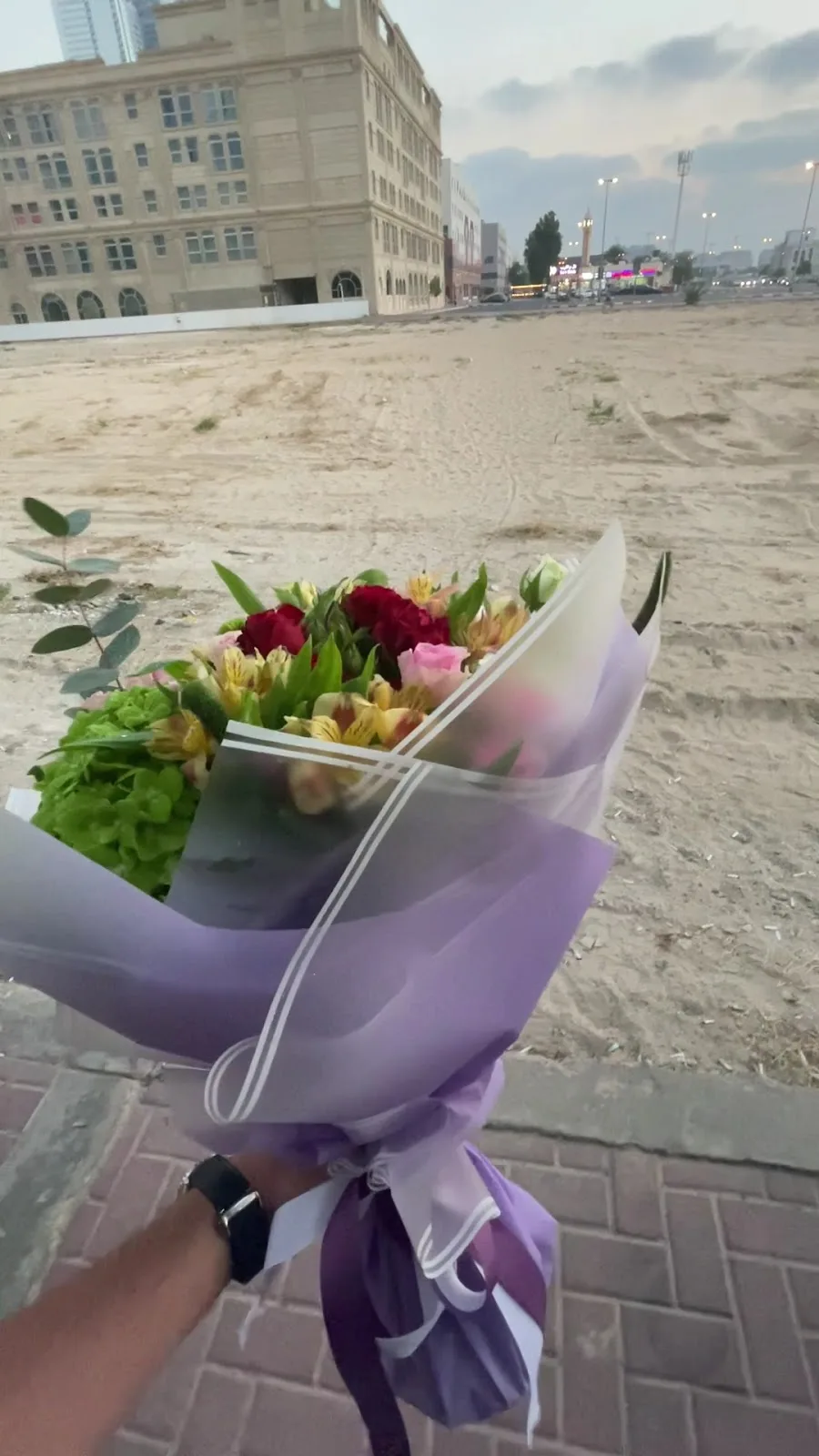 Hand holding a wrapped mixed bouquet outdoors in Dubai