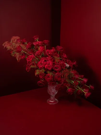 A sweeping arrangement of deep-red garden roses in a cut-glass urn, photographed against a crimson studio backdrop