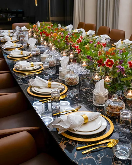 Long marble dining table styled with florals, gold cutlery and candles for an event
