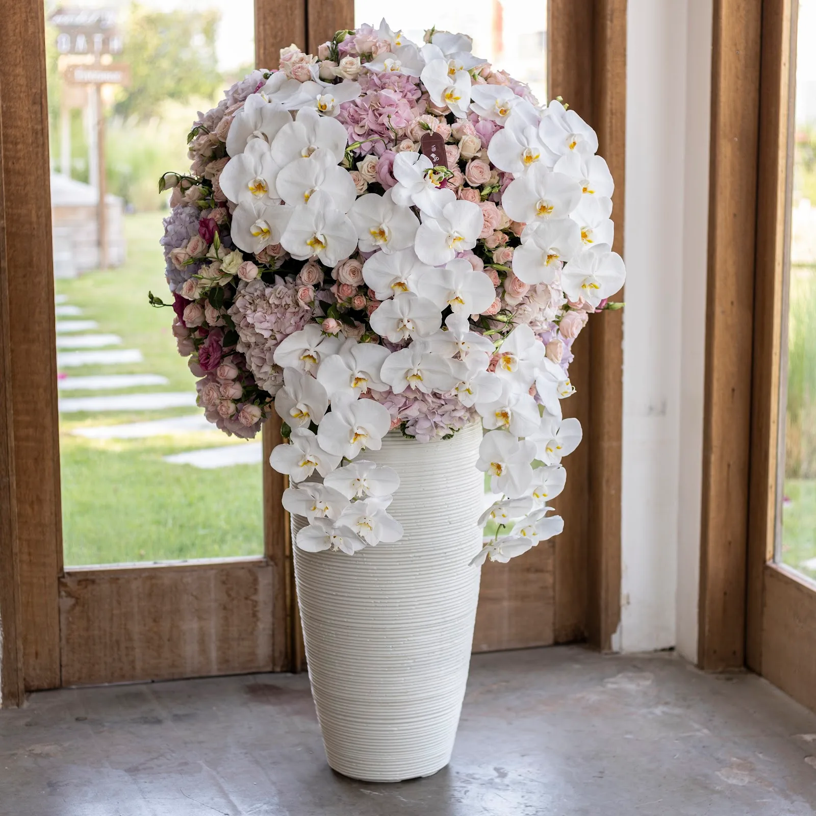 Lavish vase arrangement of white orchids and blush roses in a tall ribbed vessel