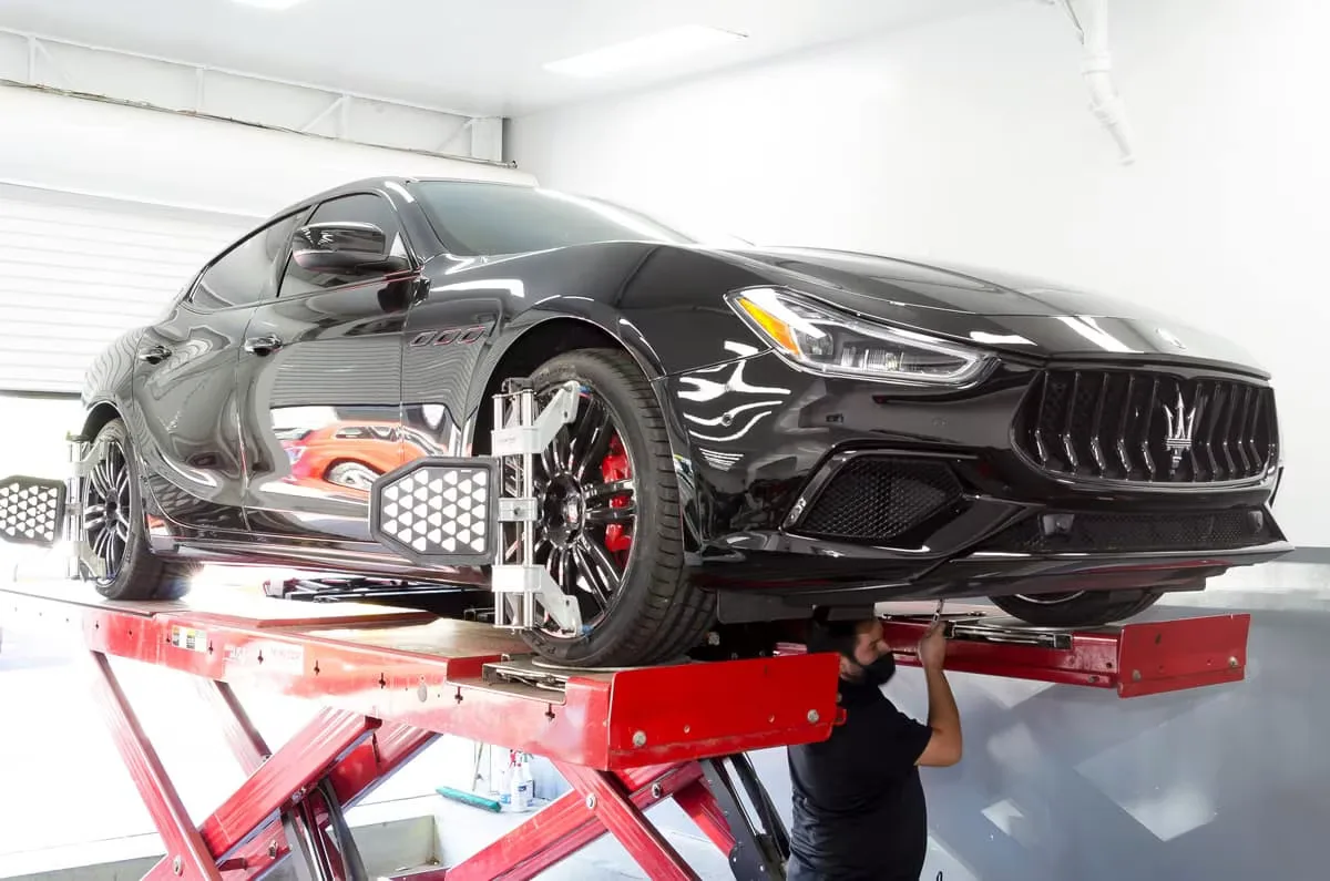 Black Maserati Ghibli raised on a scissor lift for alignment