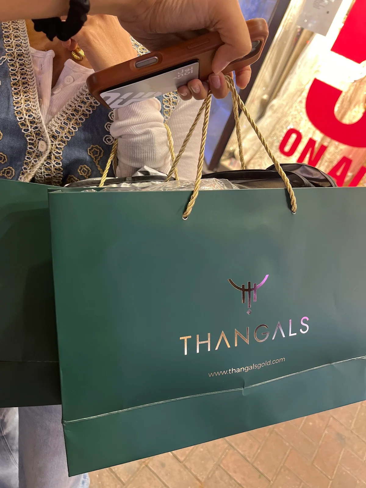 A green Thangals shopping bag with gold rope handles and foil logo