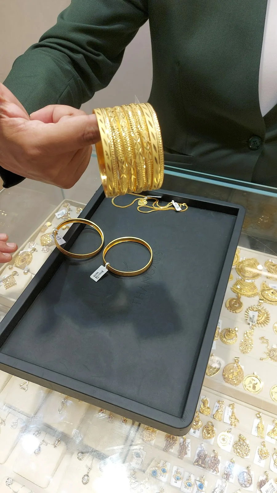 A stack of patterned gold bangles held over a display tray