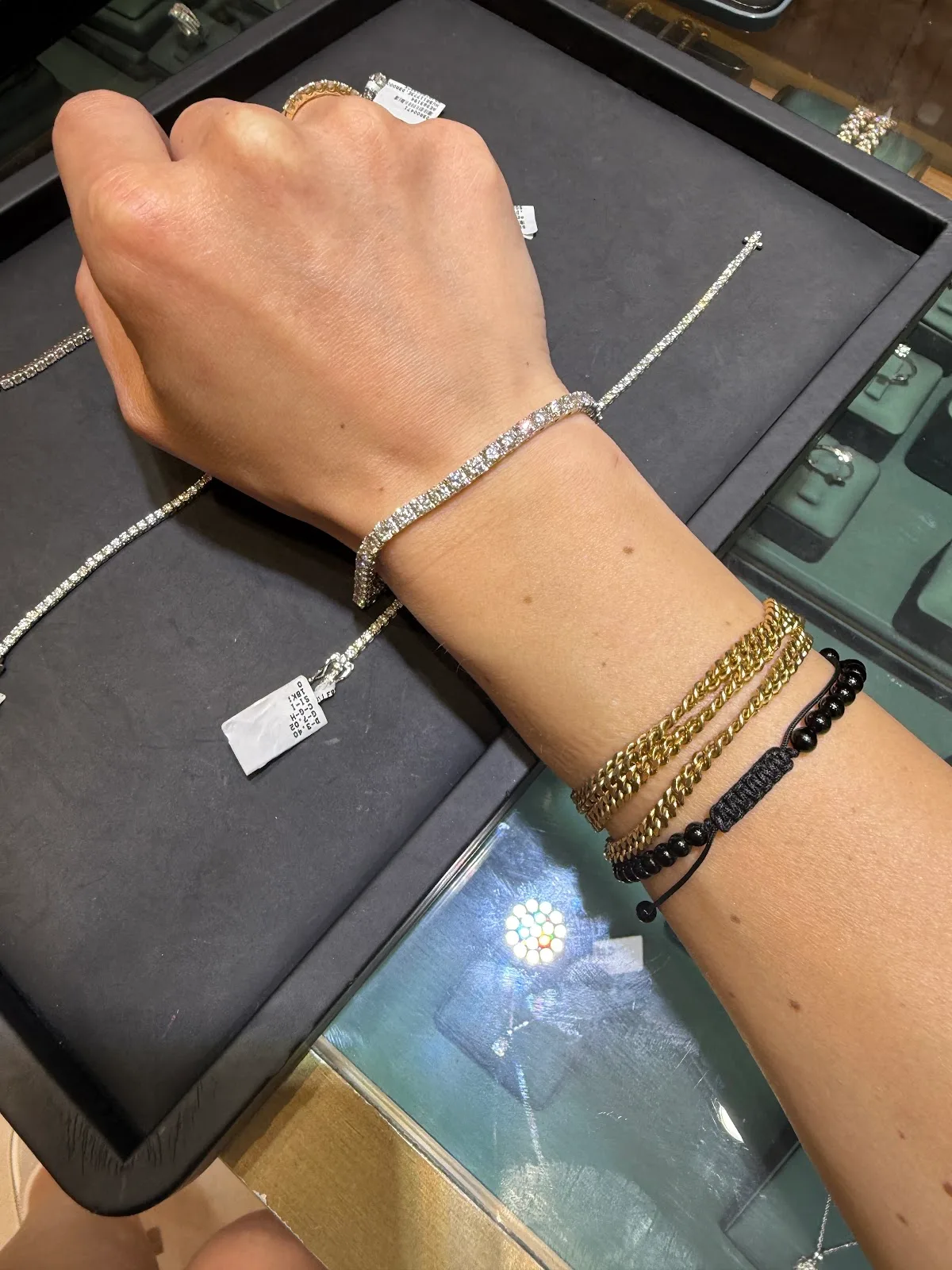 A diamond tennis bracelet and gold chain bracelets worn on a wrist