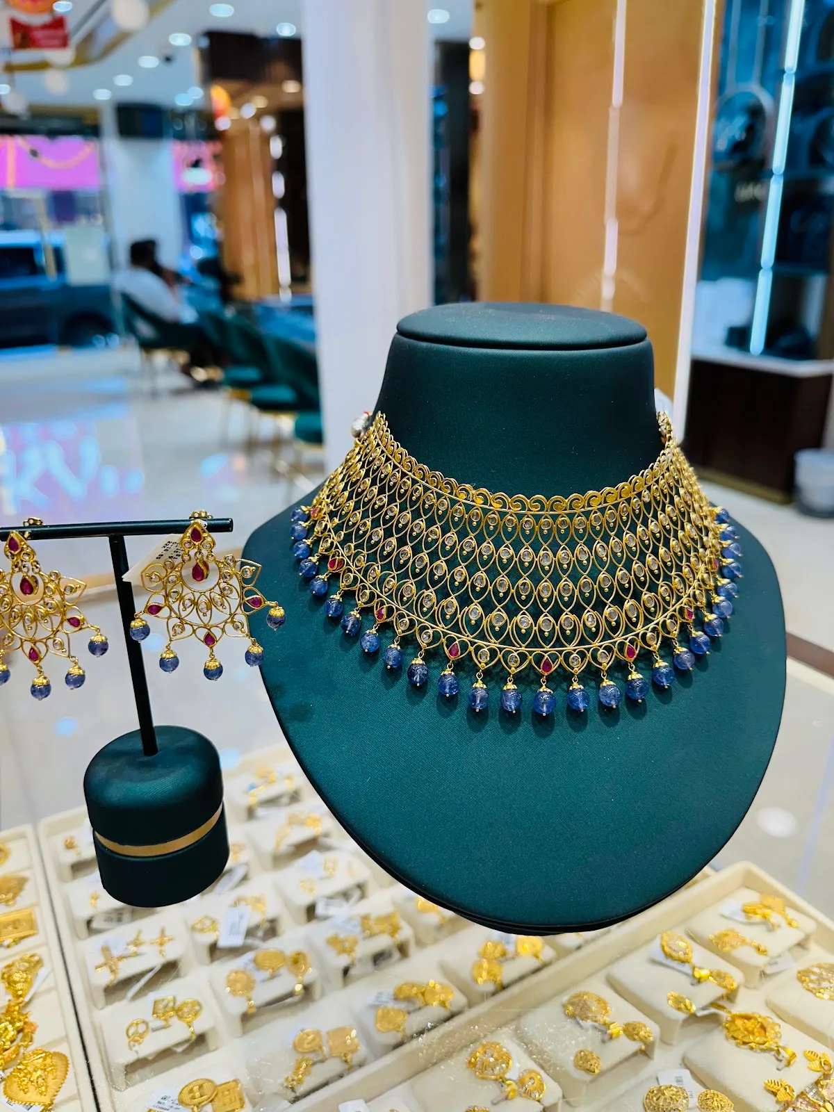 Gold choker with woven mesh detailing and blue drop beads on a display bust