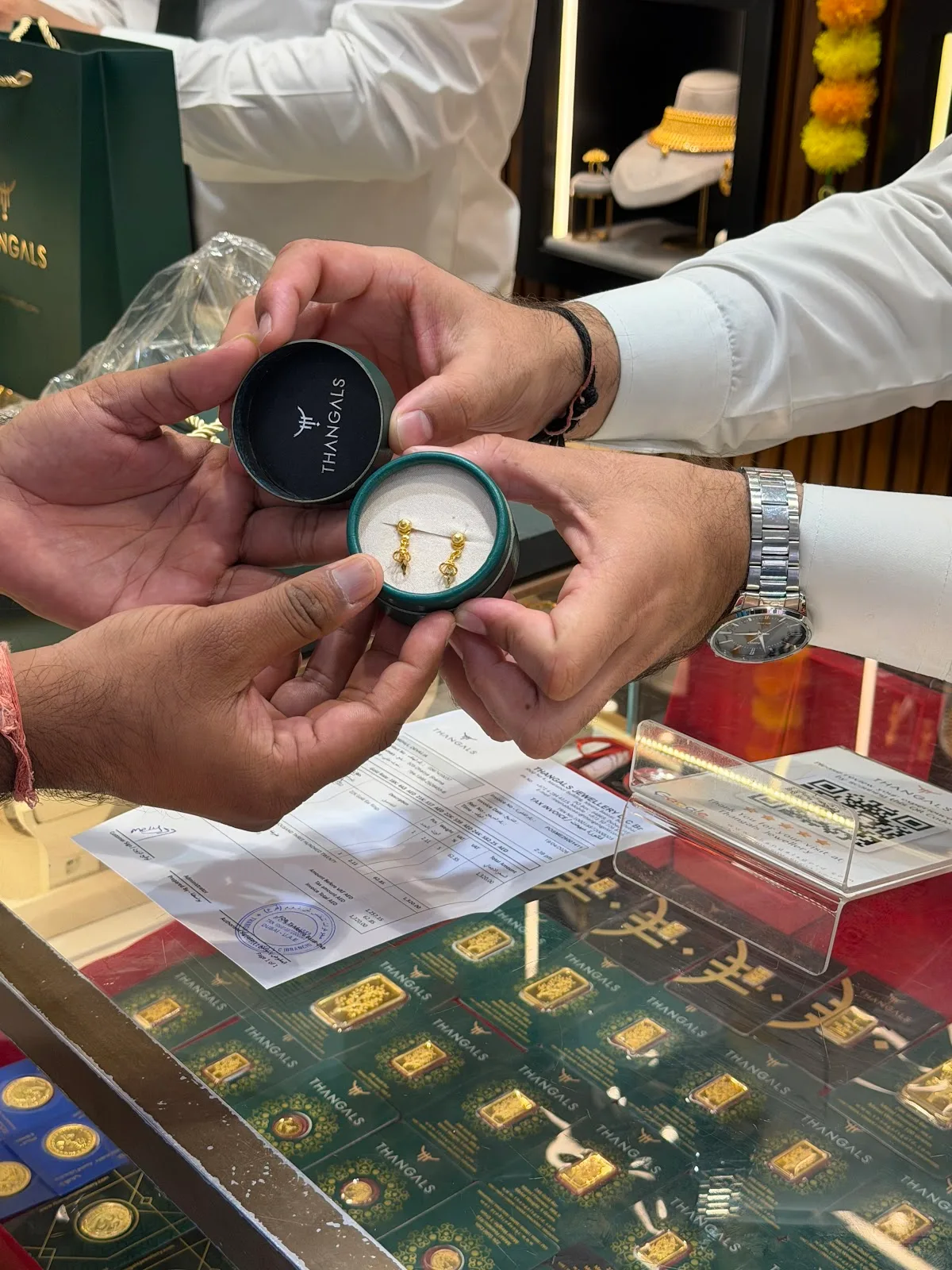 Gold earrings in a round Thangals box being handed across the counter