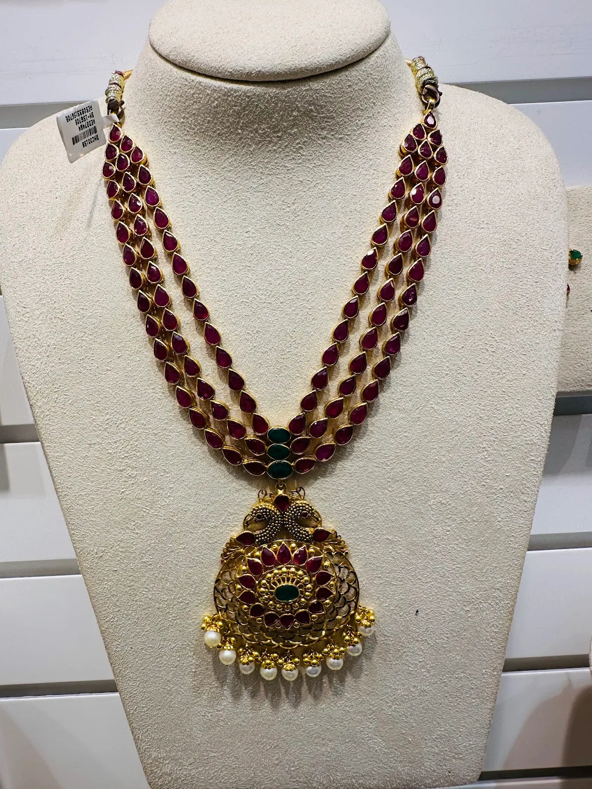 Three-strand ruby and gold bridal necklace with peacock pendant on a display bust