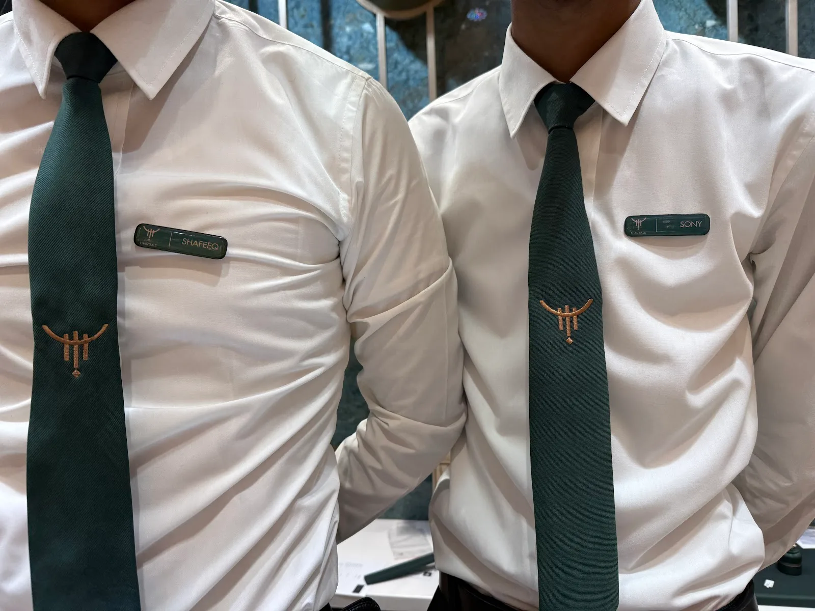 Two Thangals team members in white shirts and green ties with the brand emblem