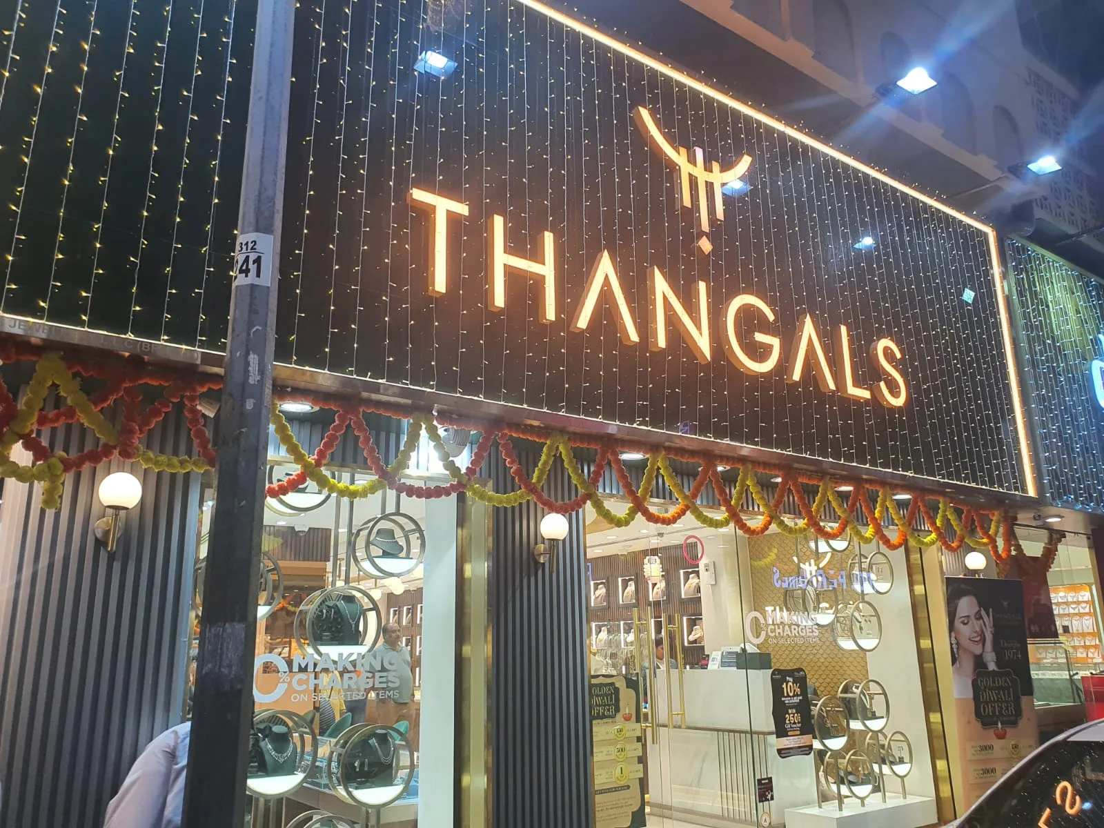 Thangals storefront at Meena Bazaar lit with warm lights and marigold garlands at night
