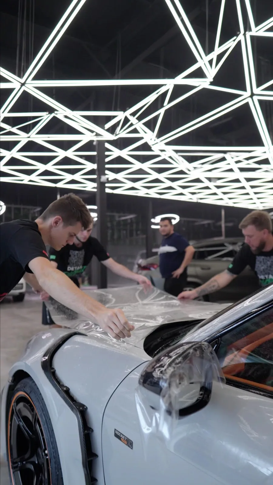 A team applying clear paint protection film to a light-grey sports car