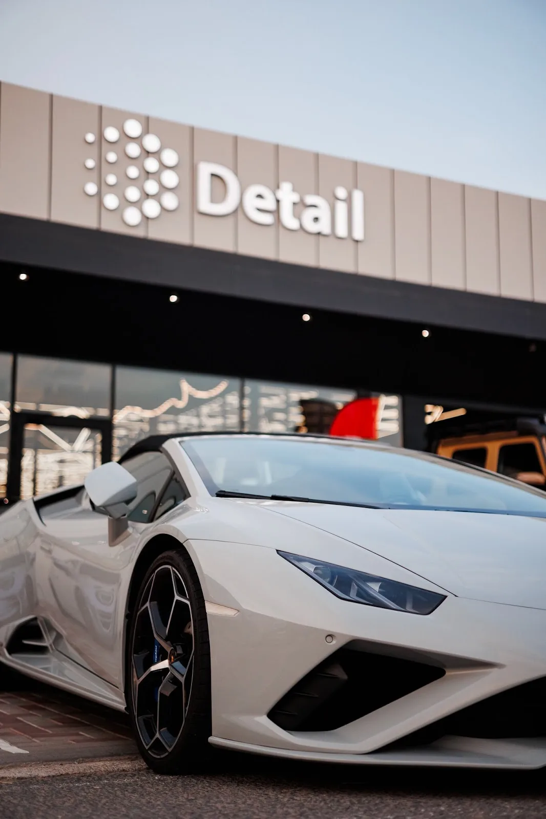 A white Lamborghini parked outside the Detail Dubai studio entrance under the illuminated Detail sign