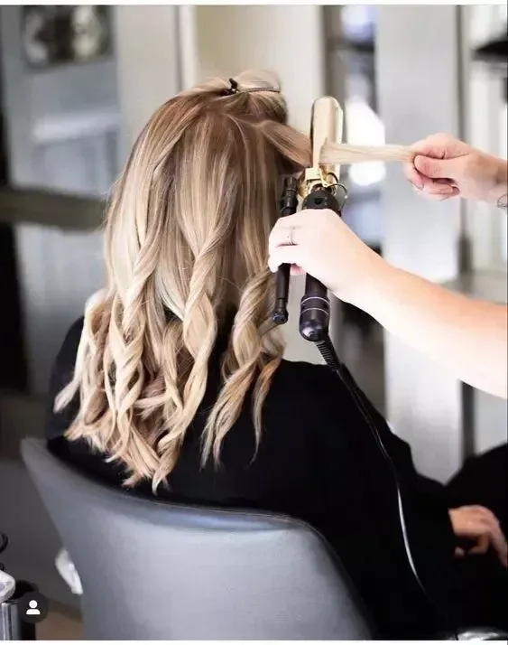 A stylist curling a client's hair at the styling chair
