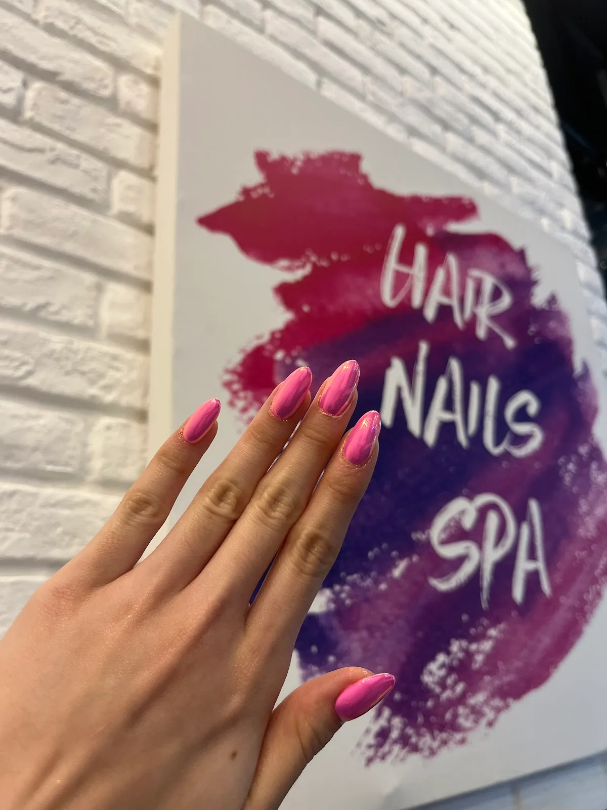 A manicured hand with glossy pink nails beside the salon's hair, nails, spa sign