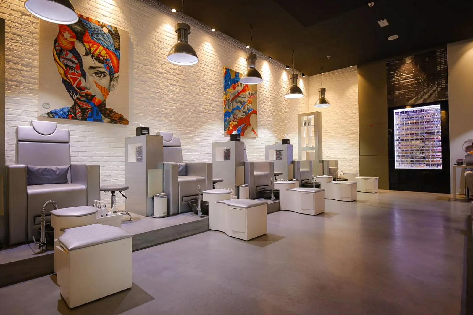 Pedicure benches beneath colourful pop-art portraits on white brick