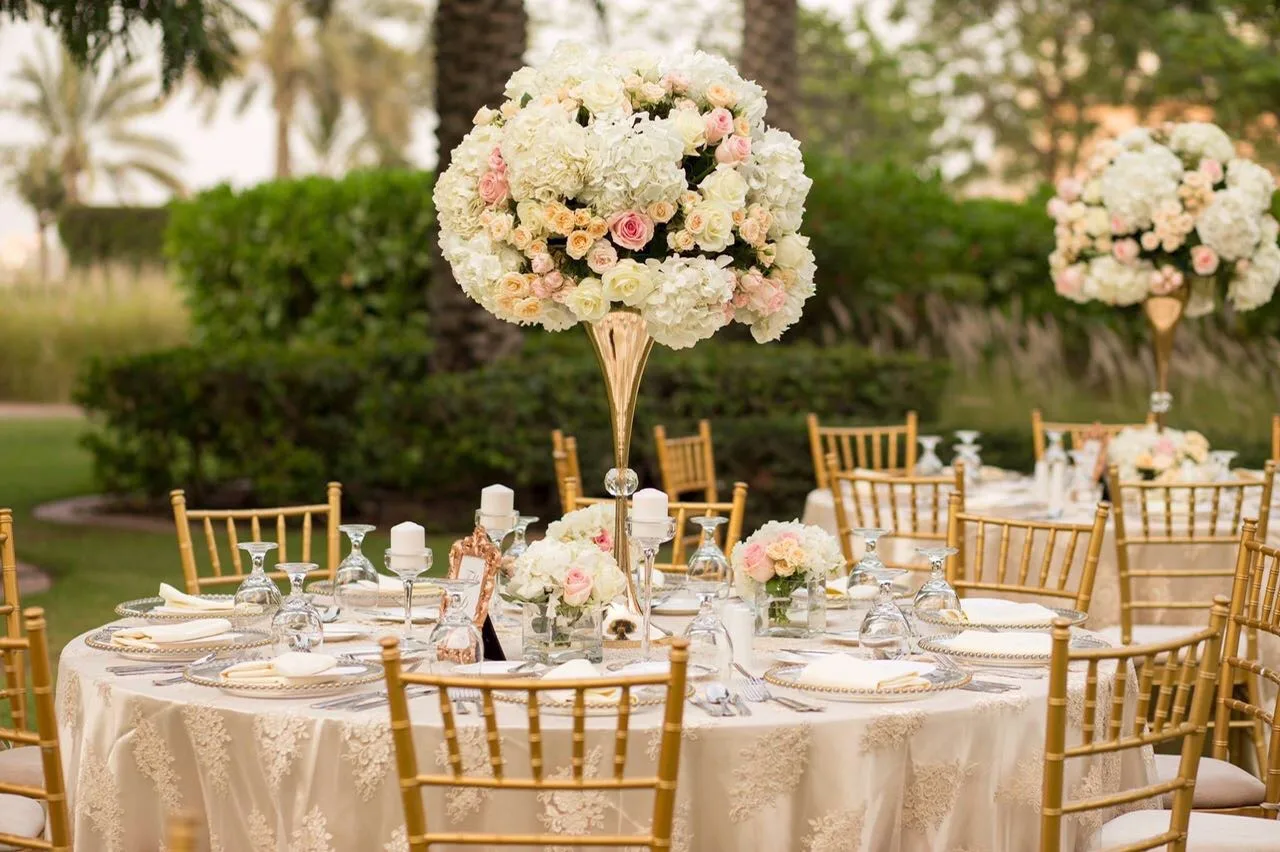 Outdoor wedding tables with tall floral centrepieces and gold chairs