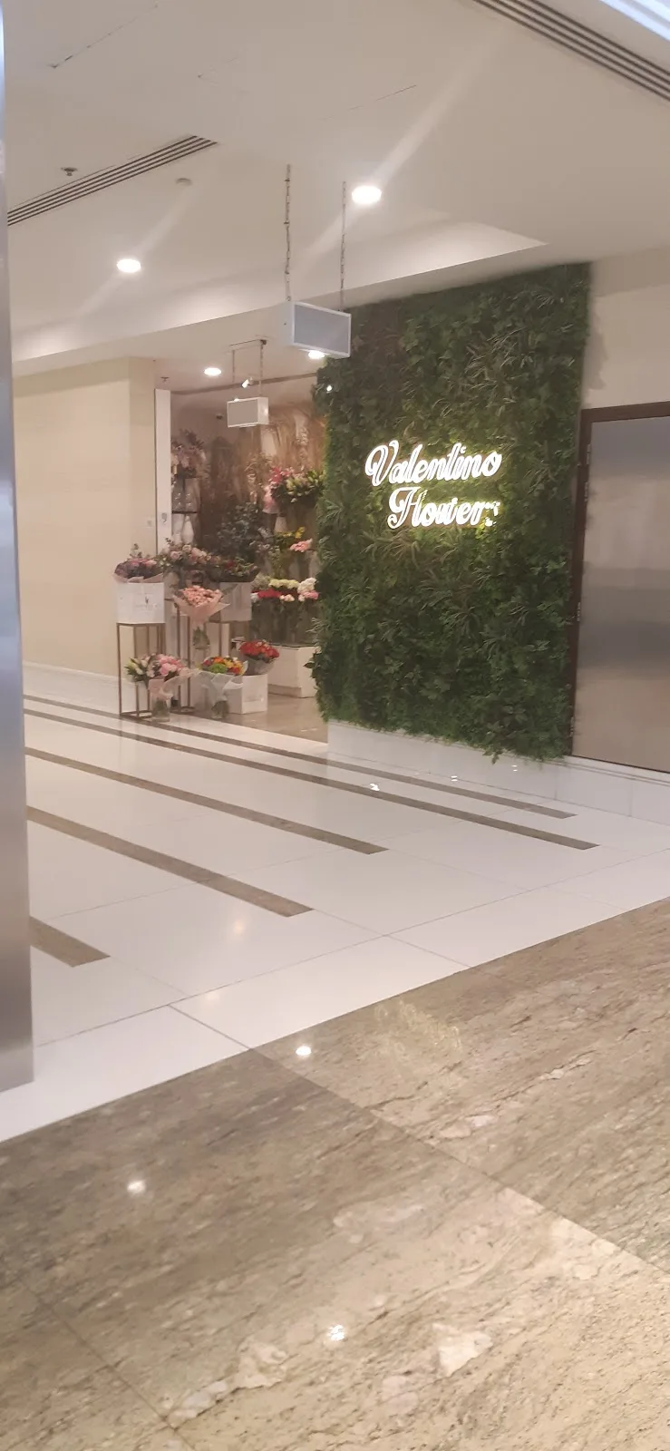 The Valentino Flowers storefront with an illuminated sign and a living green wall