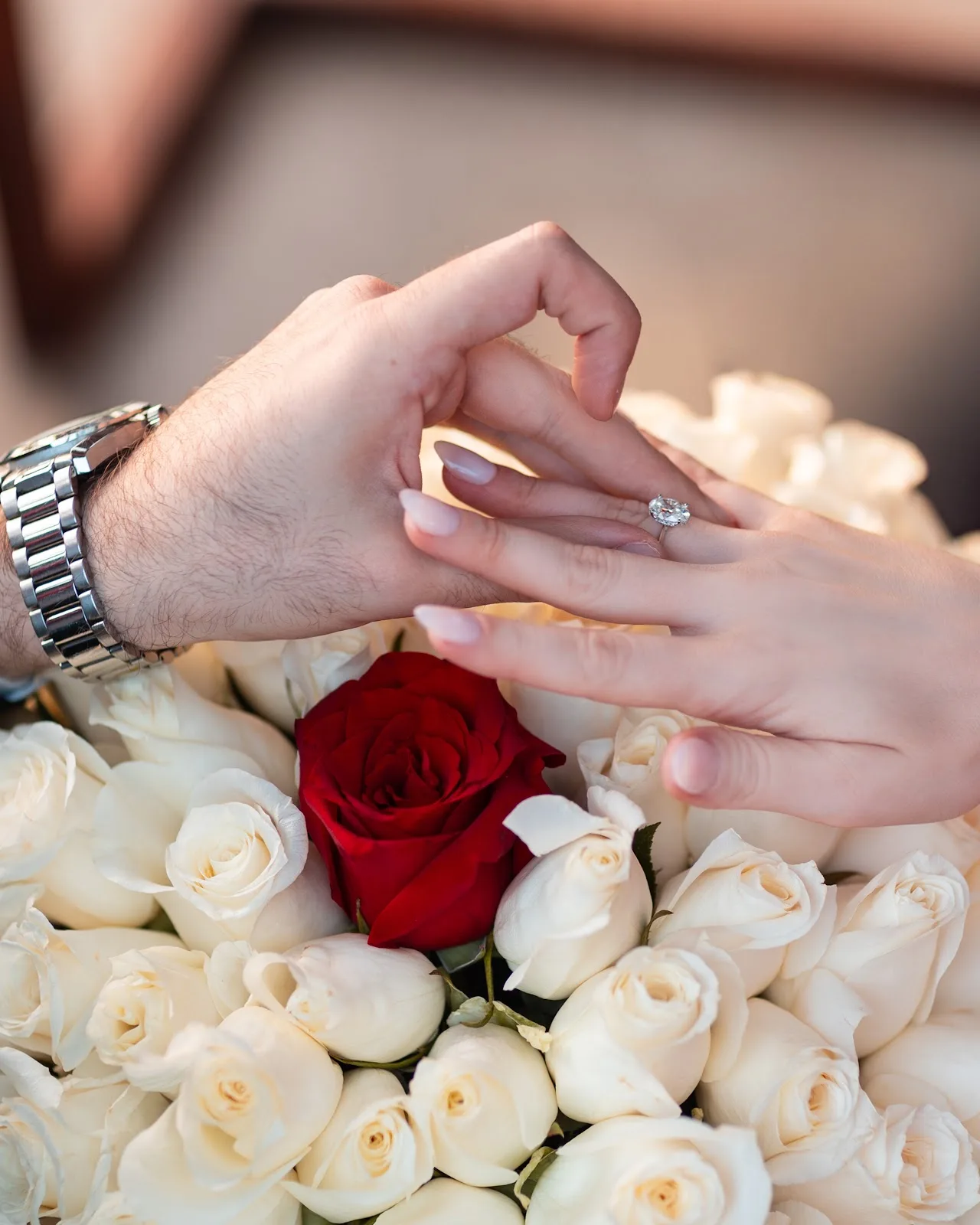 A couple's hands over roses, one wearing a diamond engagement ring