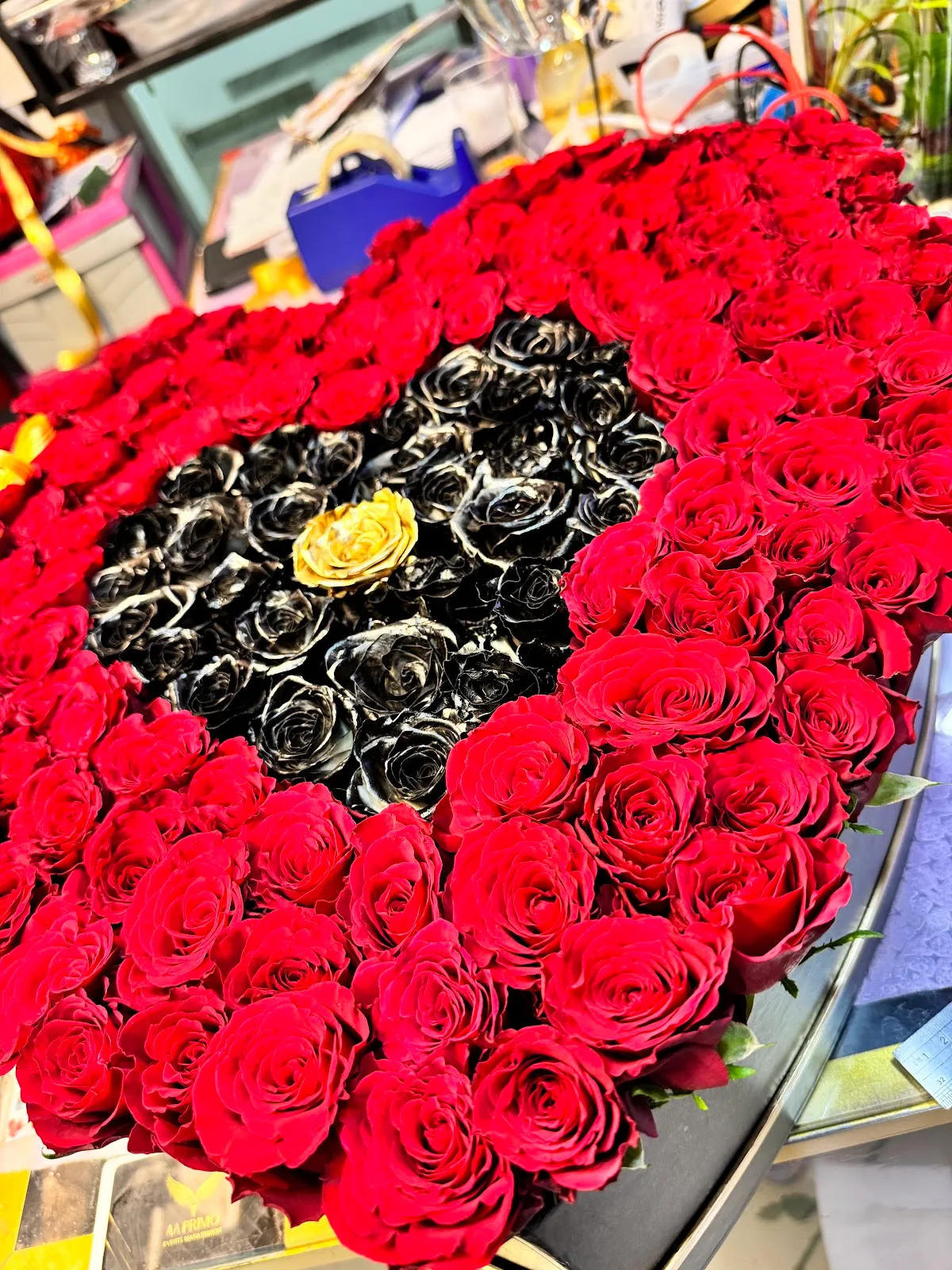 Heart-shaped arrangement of red roses with a black and gold rose centre