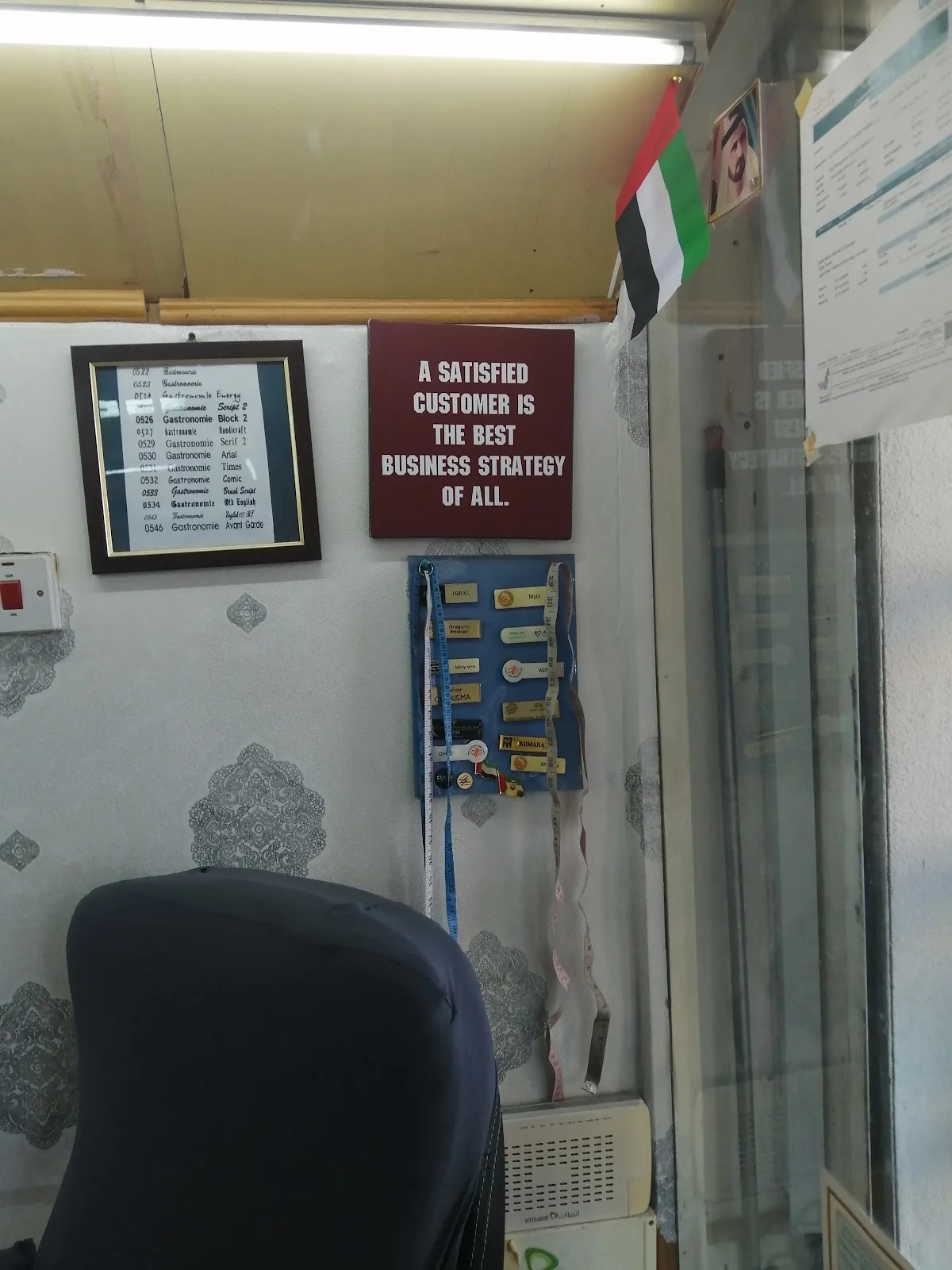 A framed sign in the shop reading ‘A satisfied customer is the best business strategy of all’, beside the tailors' measuring tapes.