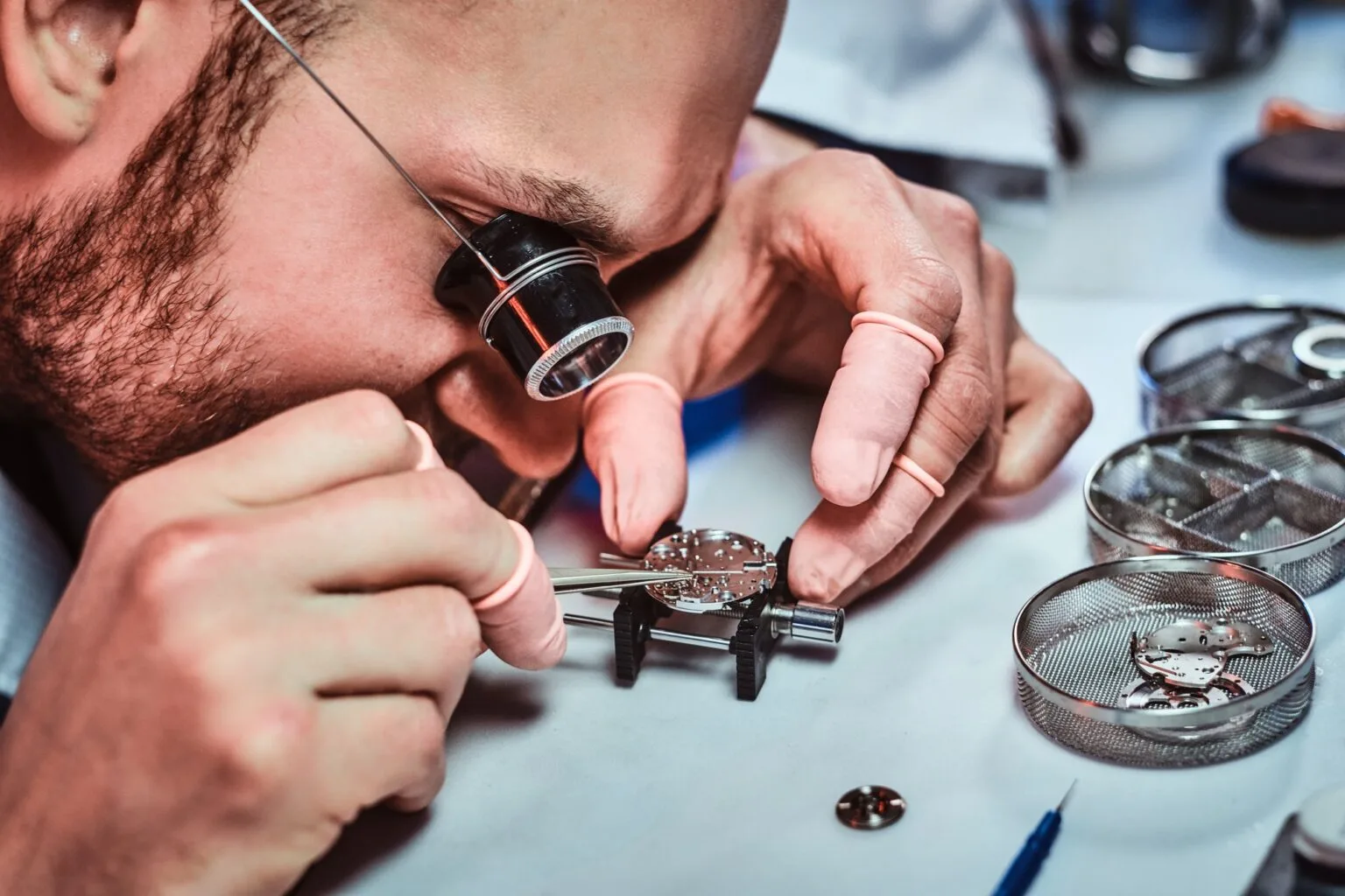 A watchmaker inspects a mechanical movement through a loupe at the bench