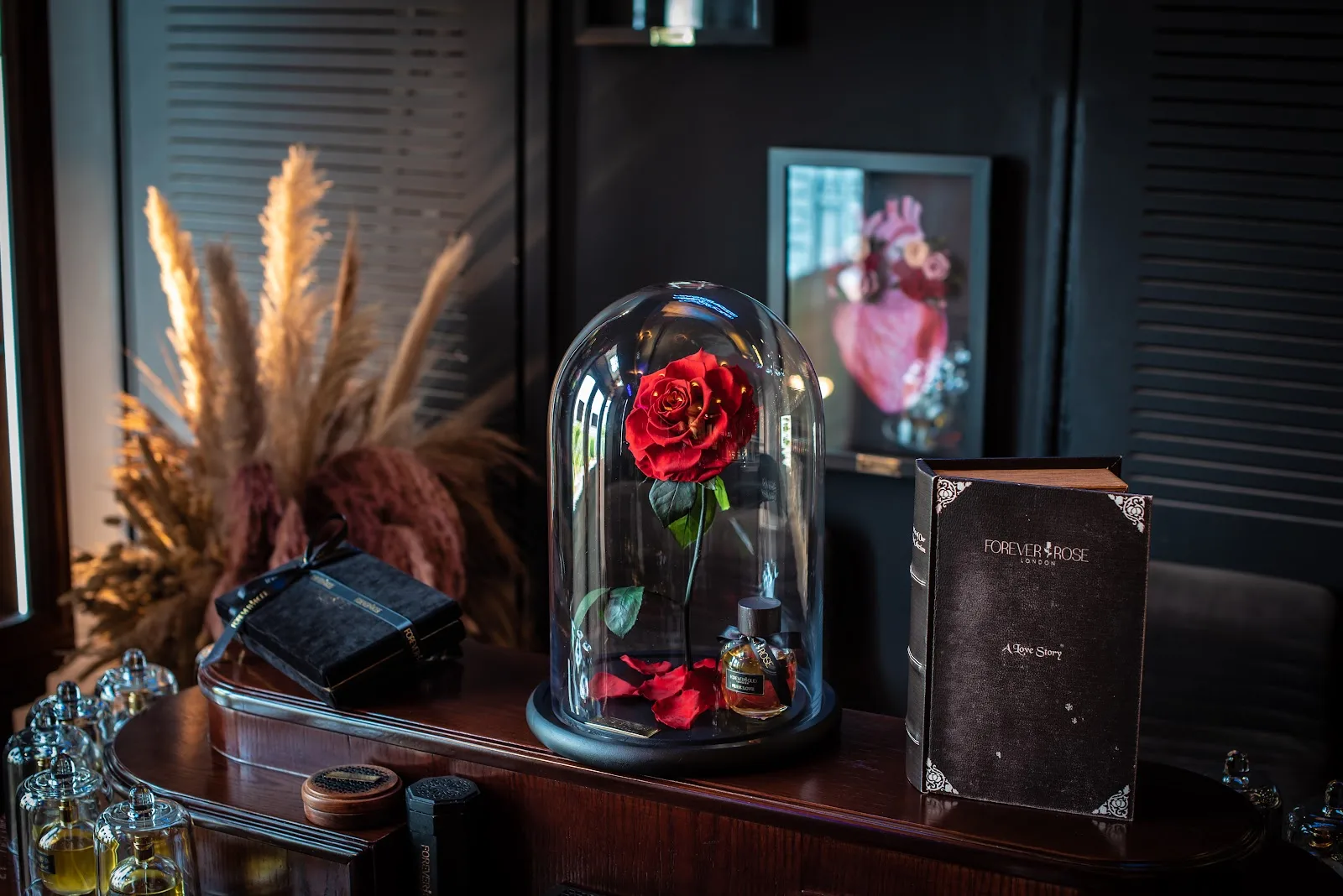 A single red preserved rose under a glass dome beside a Forever Rose love-story book
