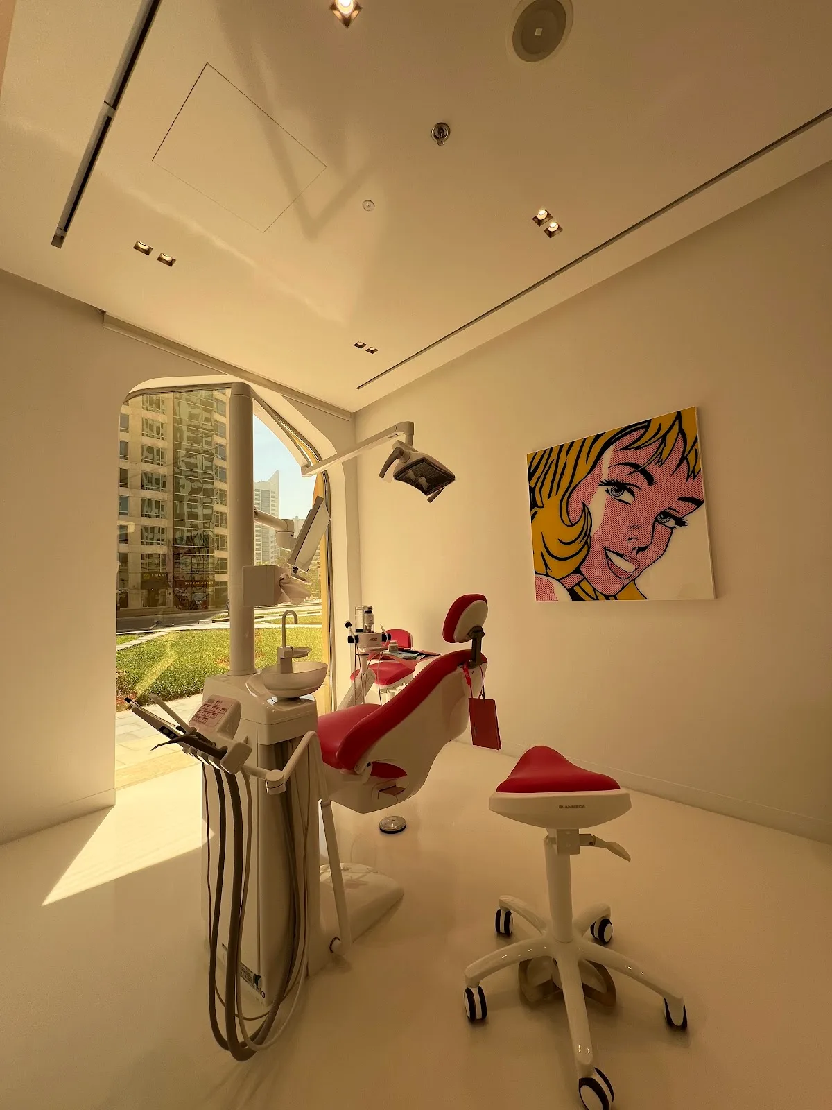 A bright treatment room at GBT Clinic with an arched window, red dental chair and pop-art canvas