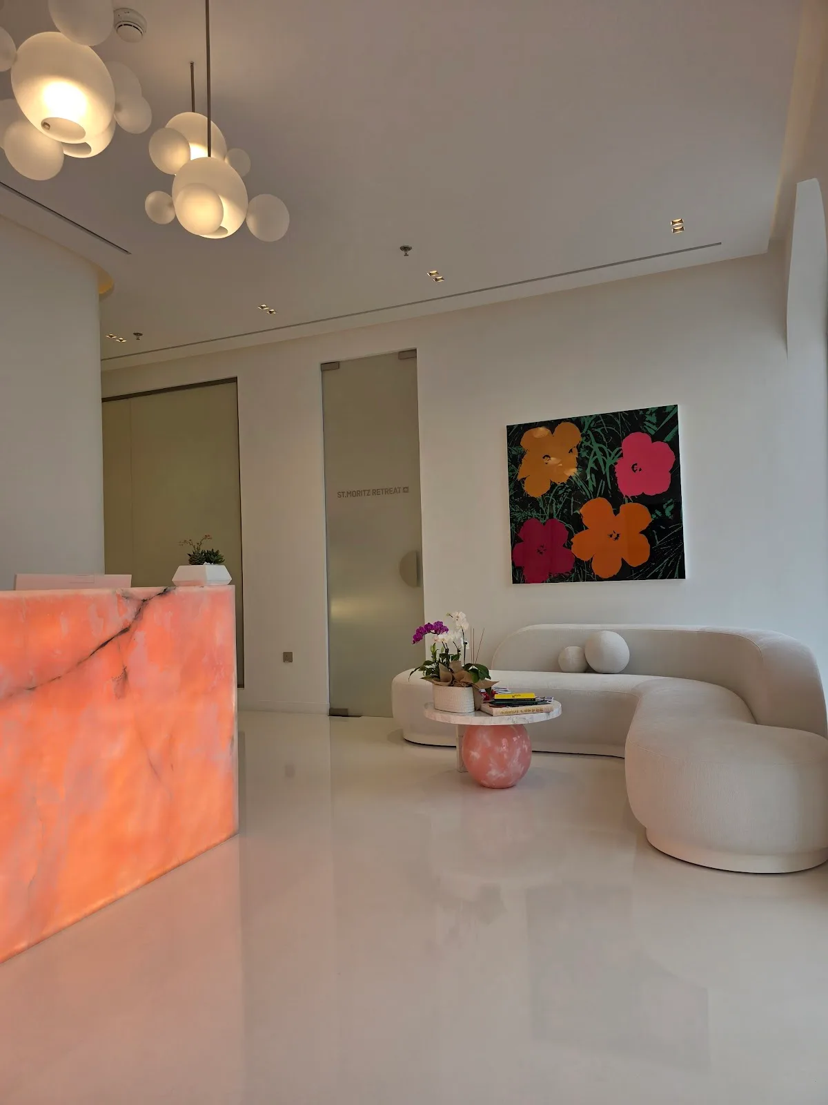 GBT Clinic reception with a backlit coral onyx desk, sculptural sofa and pop-art flowers