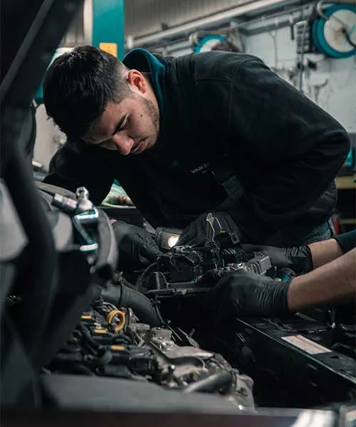 Mechanic working under the bonnet on an engine with a work light