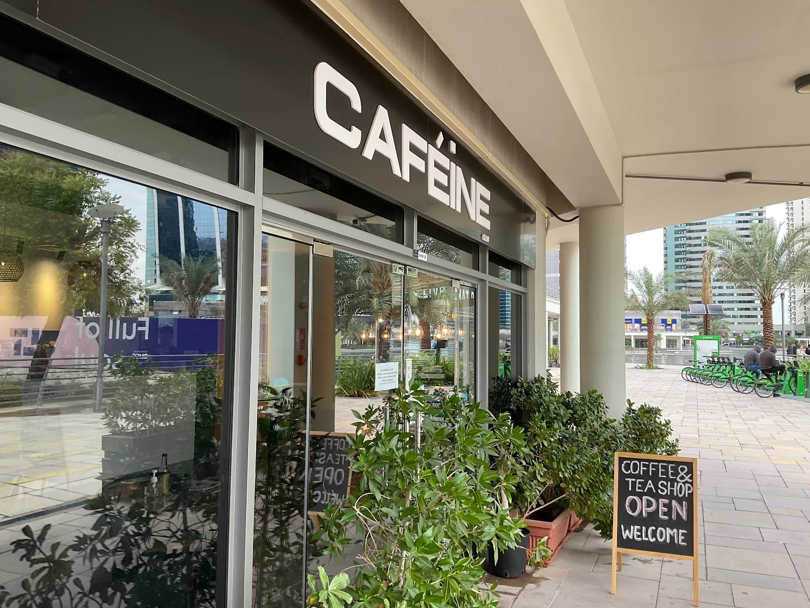 Caféine Club storefront in JLT with its CAFÉINE sign and a Coffee & Tea Shop welcome board