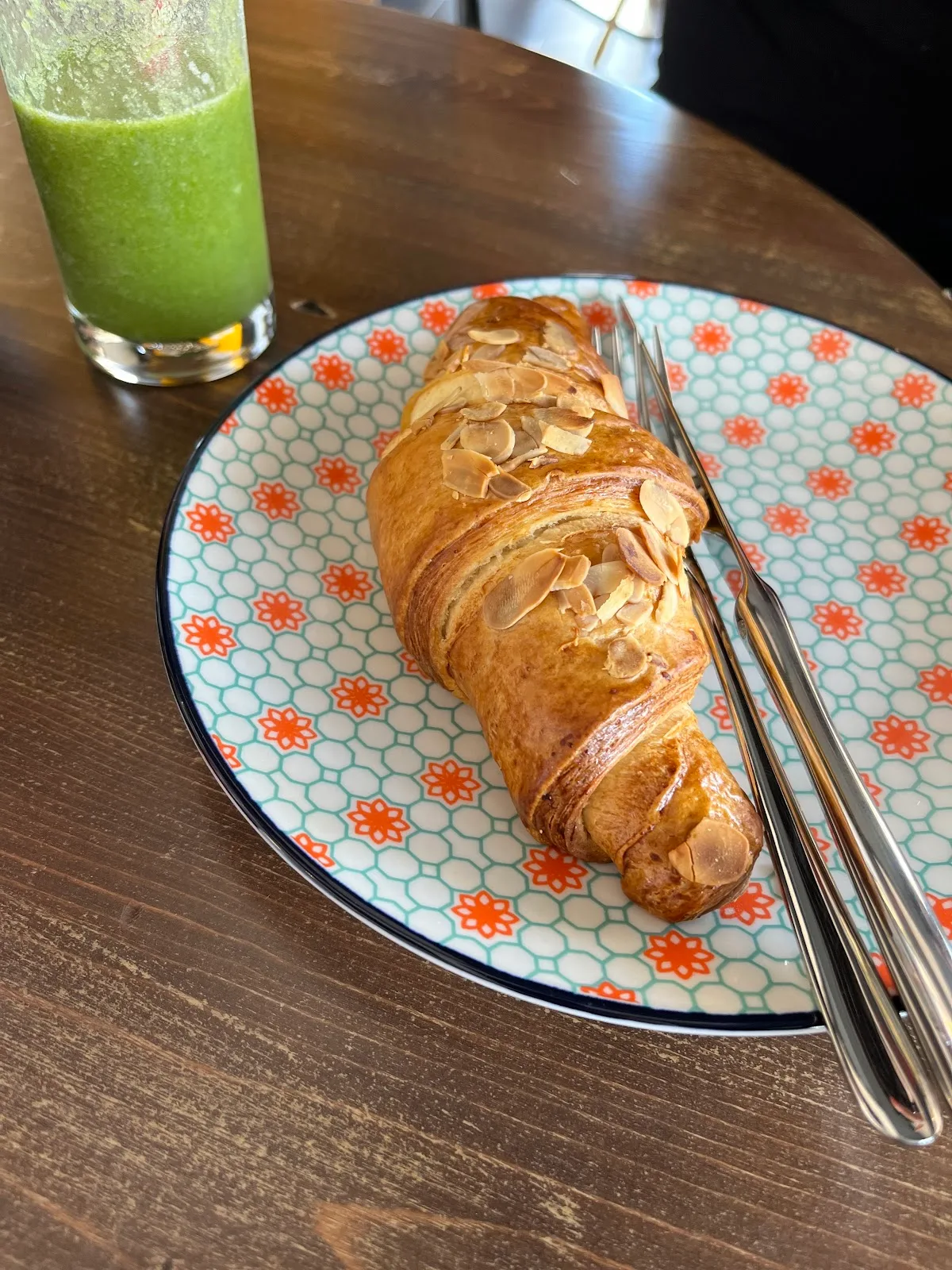 Almond croissant on a patterned plate beside a green juice