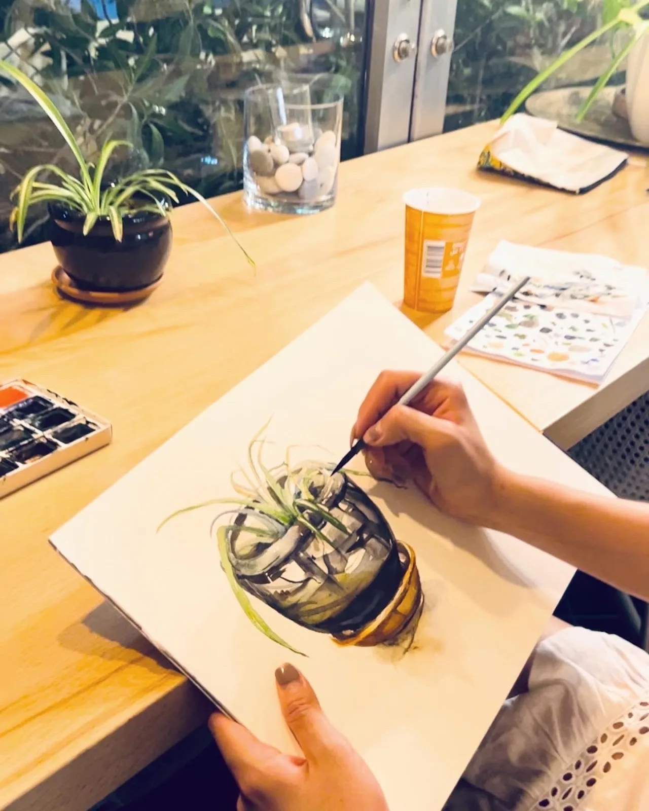 Hands painting a watercolour study of a plant during a workshop at the café