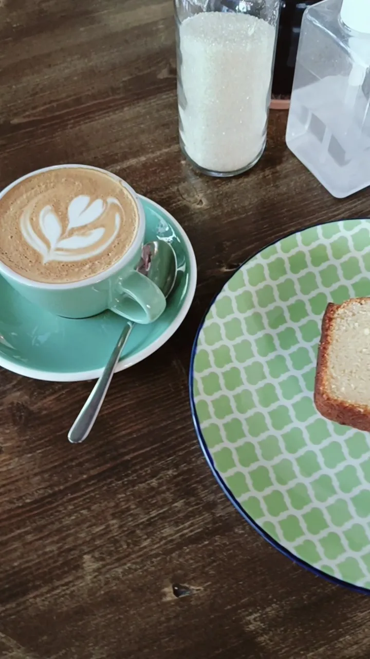 Flat white in a mint cup beside a slice of cake on a patterned plate