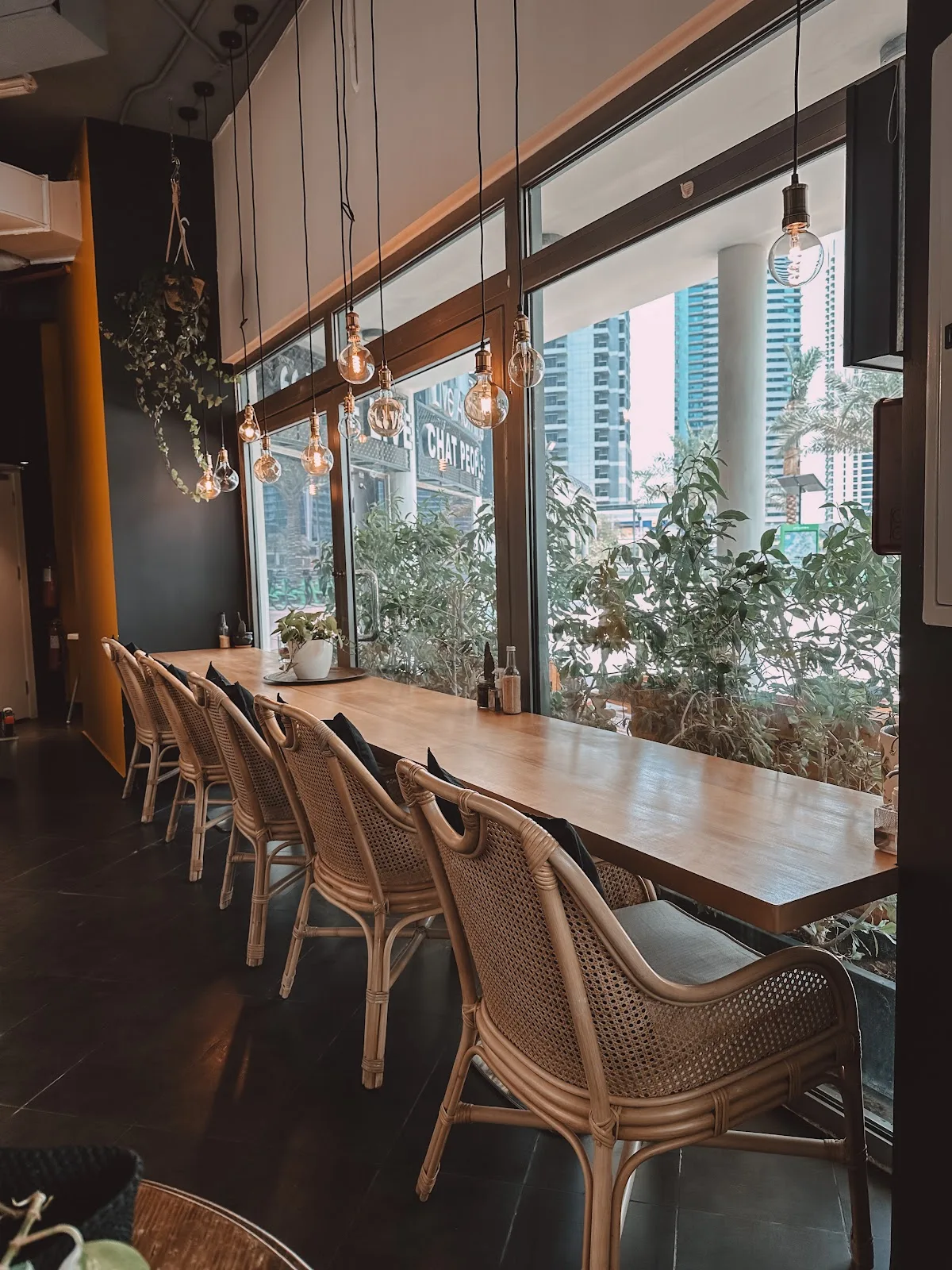 Long communal window bar lined with rattan chairs and pendant Edison bulbs