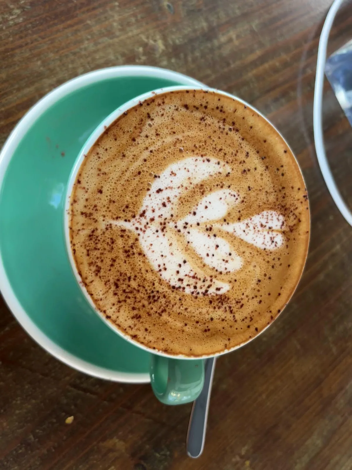 Cappuccino with leaf latte art and a dusting of cocoa in a green cup