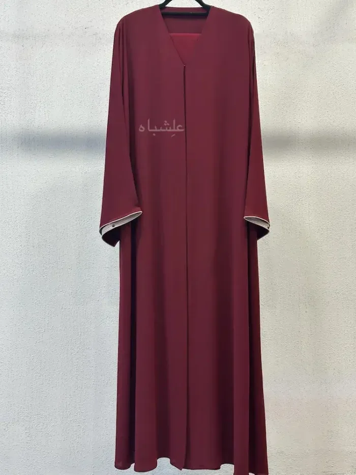 Deep maroon open-front abaya with a contrast piped trim on a hanger