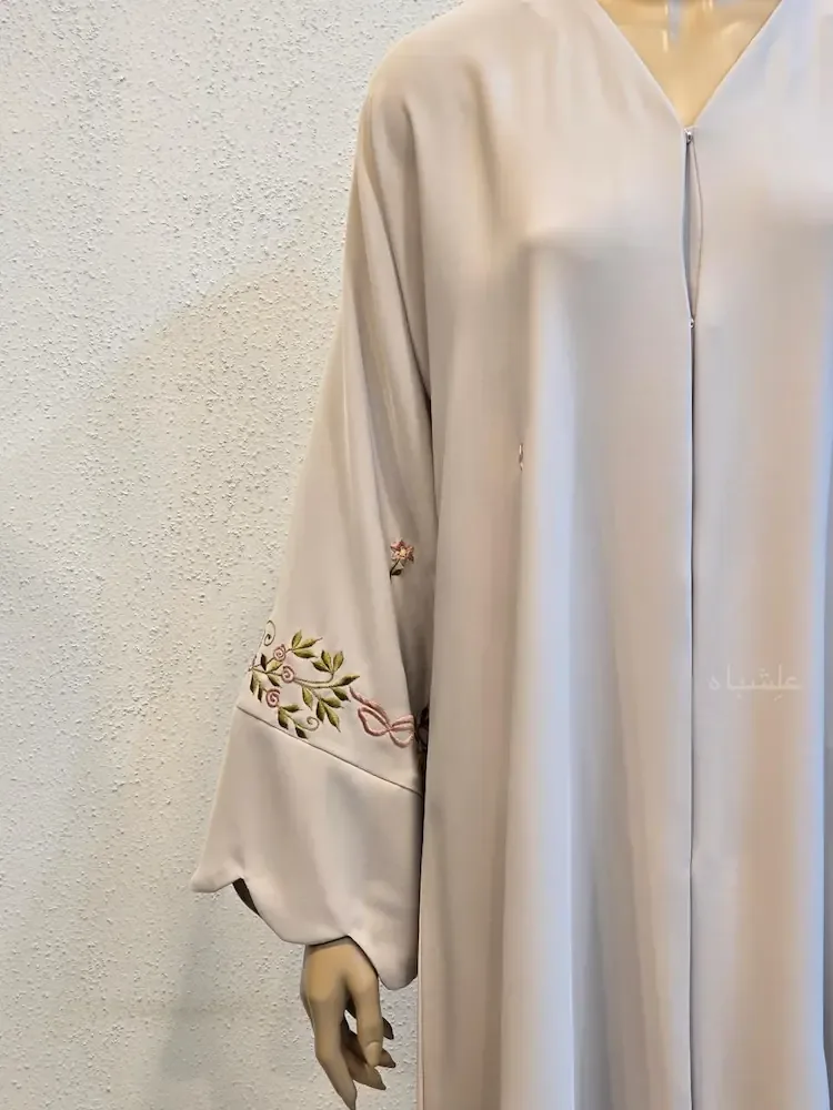 A cream abaya on a mannequin with delicate floral leaf embroidery along the sleeve cuff
