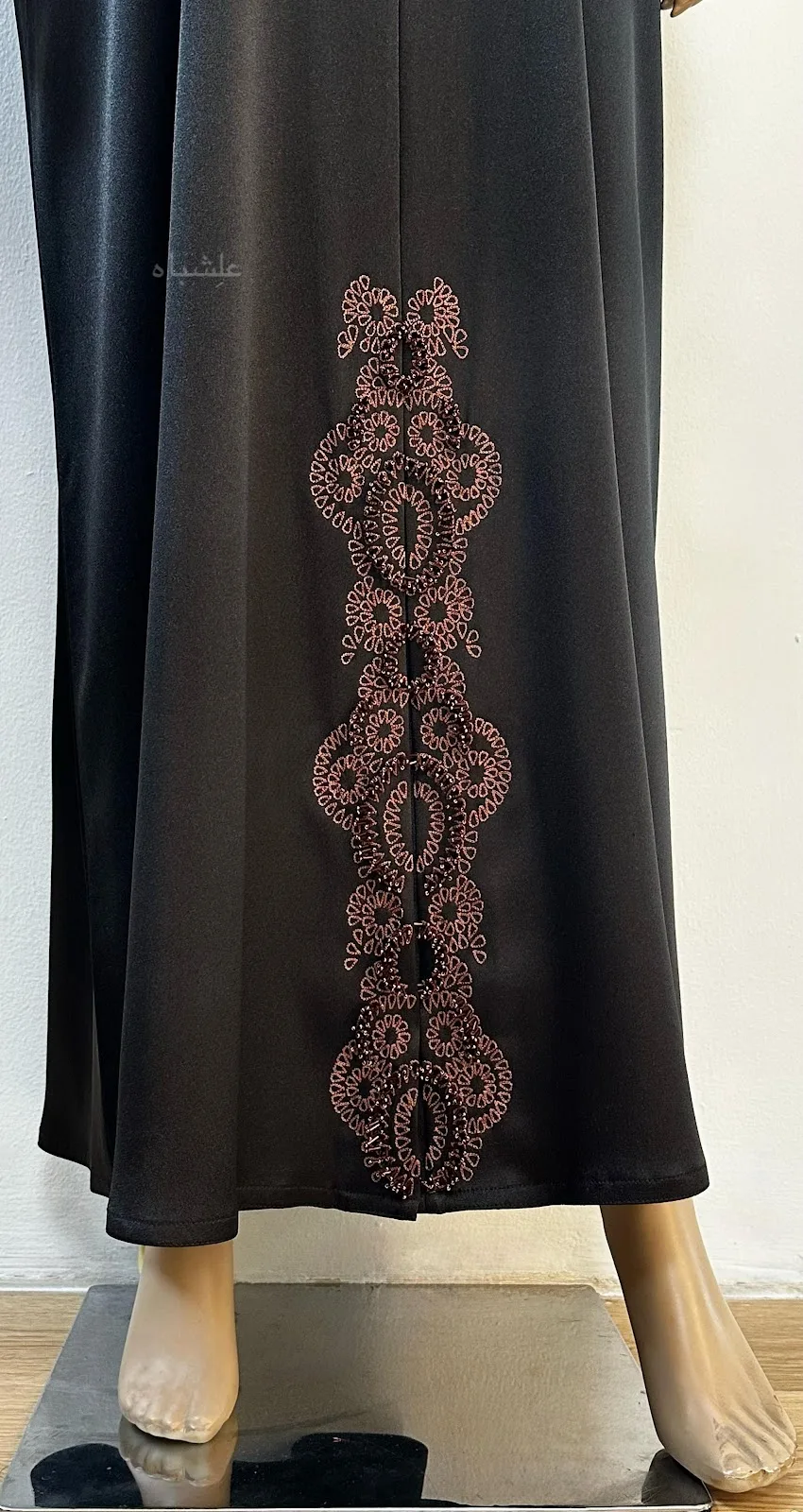 A craftsperson hand-stitching gold and beaded detail onto deep red fabric on a work table