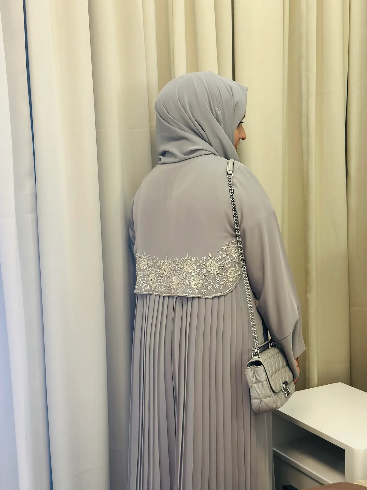 Neutral and earthy-toned abayas hanging on a brass rail beside woven baskets