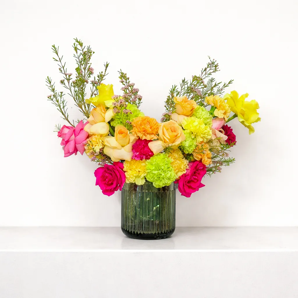 A colourful mixed flower arrangement in a green glass vase