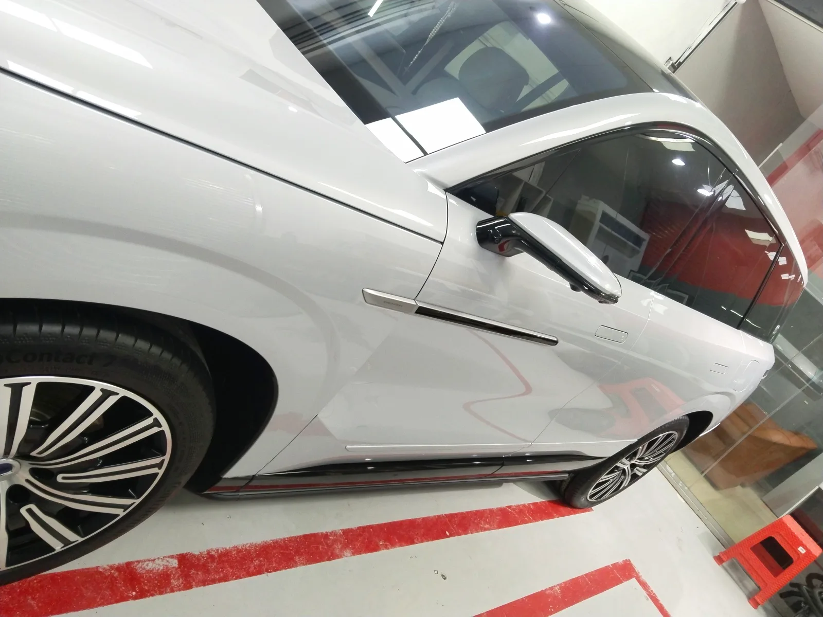 Close detail of a clean white car's side panel and wheel in the workshop