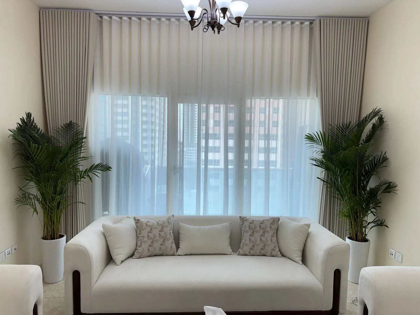 Layered sheer and taupe curtains framing a living room window with potted palms