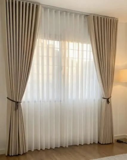 Close detail of beige pinch-pleat curtains over white sheers with a tieback