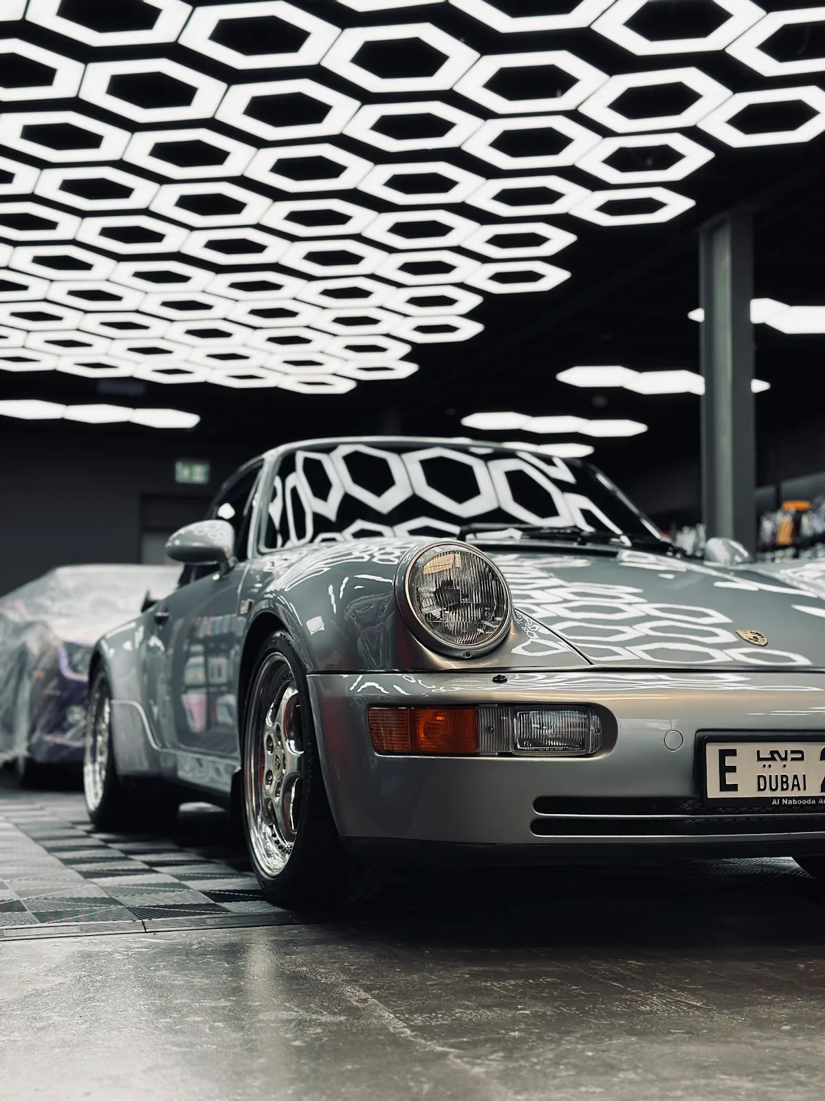 A silver Porsche 911 detailed to a mirror finish beneath the hexagon lighting at Gulf Detailing, Al Quoz